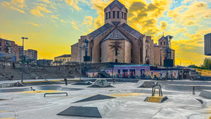 Skateboarding in Armenia: a concrete skatepark with ledges and banks in front of a large stone cathedral at golden hour. Photo by Mike Boisvert / The Skate Nomad