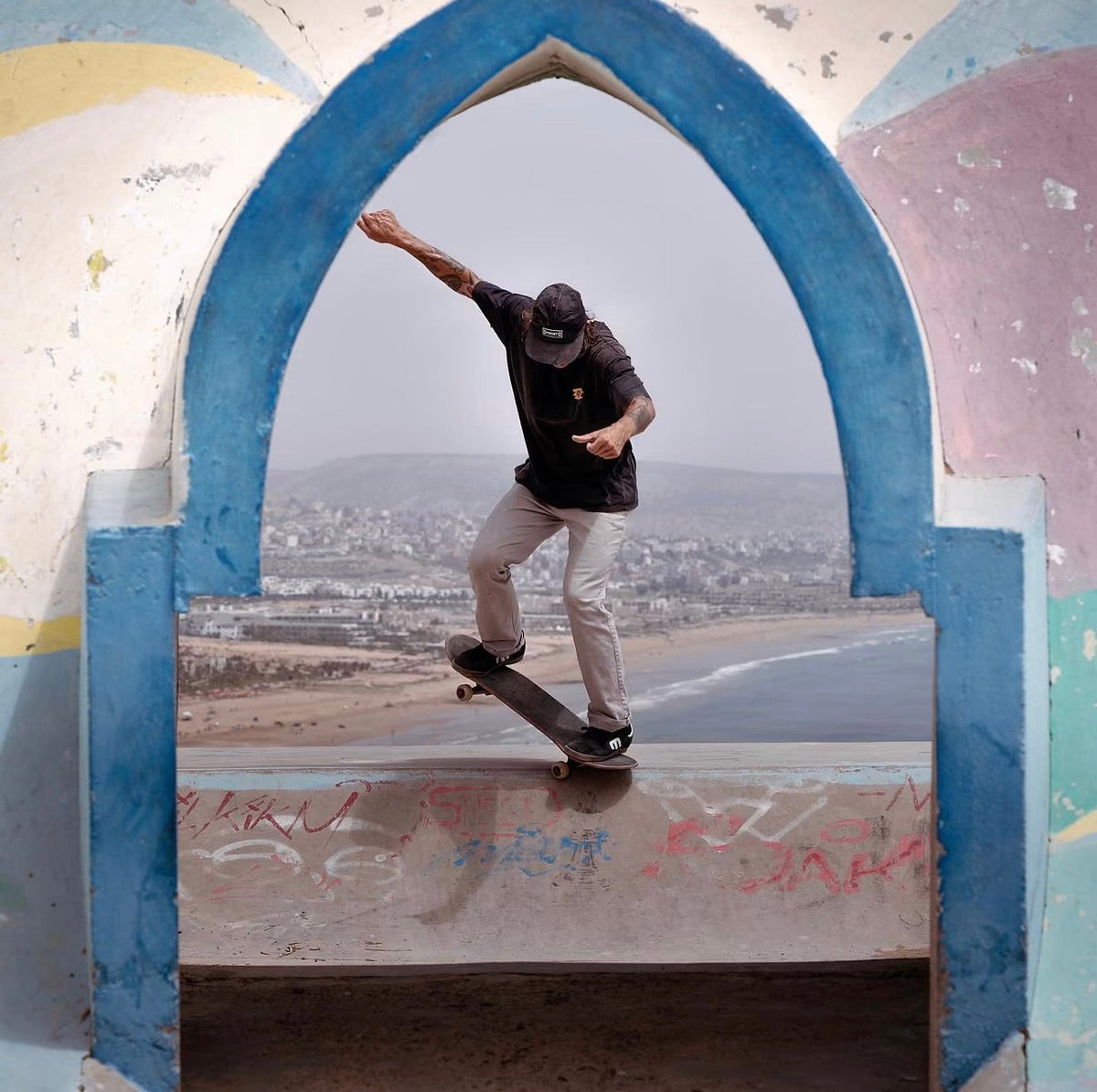 Skateboarding in Morocco: a skater rides a ledge framed by a blue arch, the Atlantic coast below. Photo by Mike Boisvert / The Skate Nomad