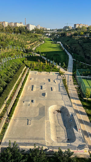 Skateboarding in Georgia: aerial view of a concrete skatepark with a long bowl and street obstacles in a green park below the city. Photo by Mike Boisvert / The Skate Nomad