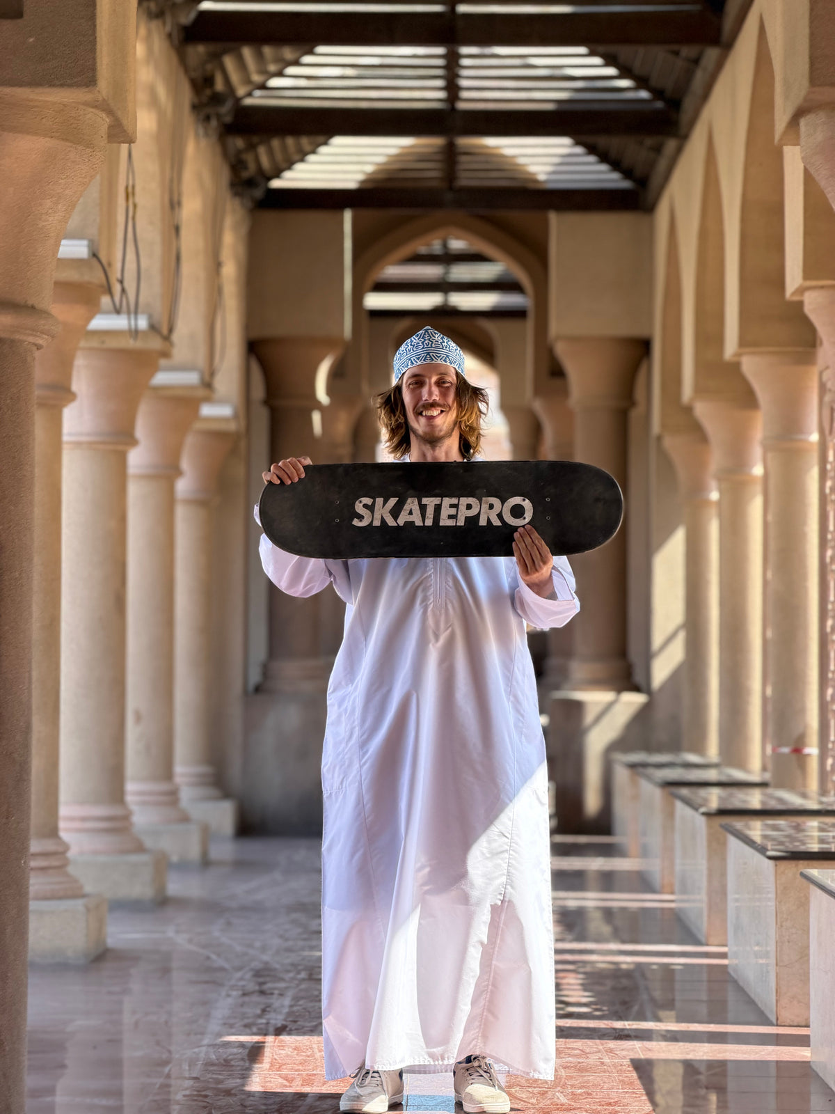 Muscat, Oman: Mike Boisvert in a dishdasha holds up his board. Photo by Mike Boisvert / The Skate Nomad