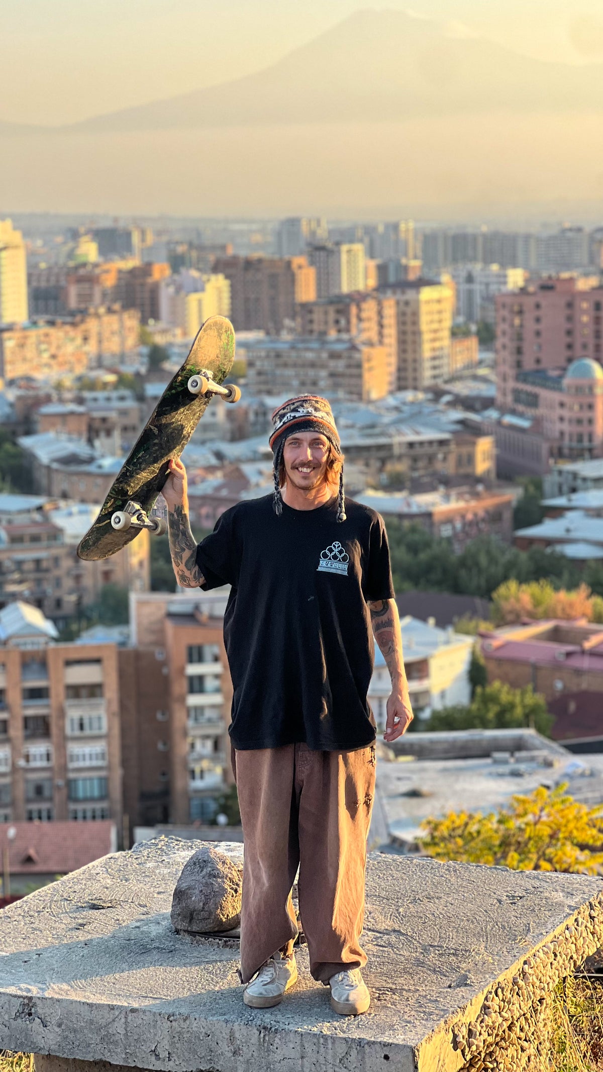 Armenia: Mike Boisvert holds his skateboard up on a rooftop ledge above the city's apartment blocks. Photo by Mike Boisvert / The Skate Nomad