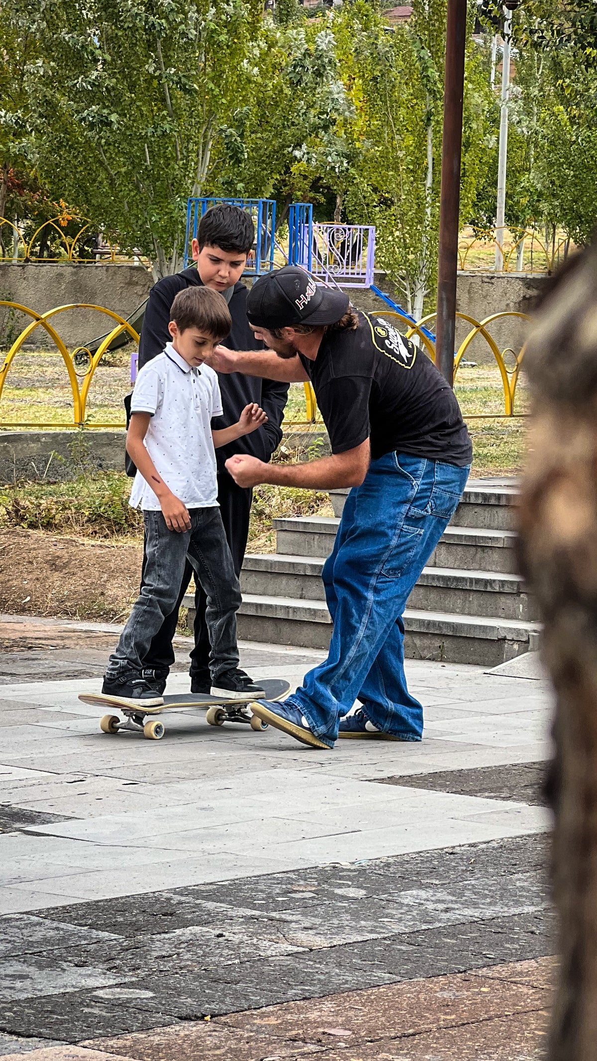 Skateboarding in Armenia: a skater helps a young boy balance on a skateboard on a plaza. Photo by Mike Boisvert / The Skate Nomad