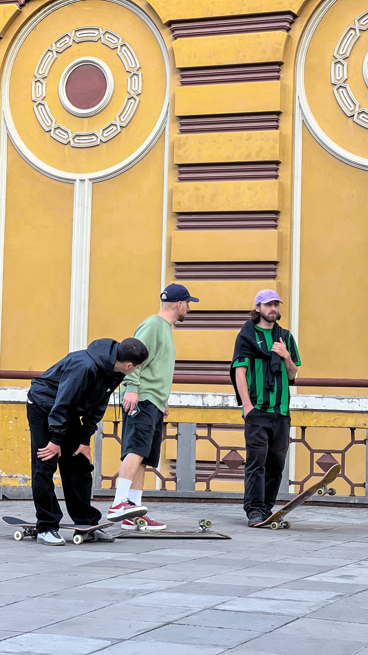 Skateboarding in Georgia: three skaters chat with their boards on a plaza in front of an ornate yellow building. Photo by Mike Boisvert / The Skate Nomad